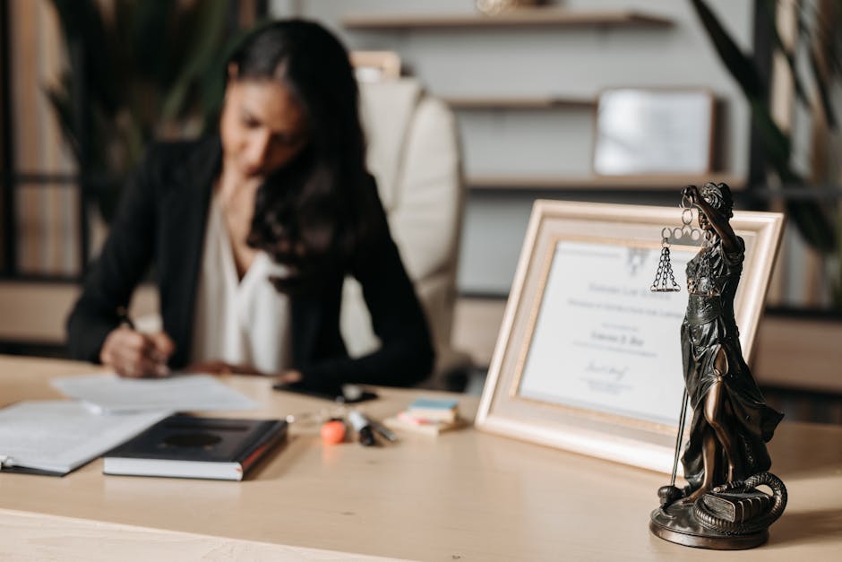 Focused woman writing at desk with Lady Justice figurine and certificate in office
